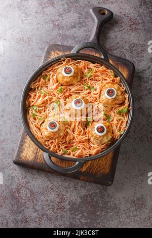 Spaghetti con salsa di pomodoro e polpette con occhi divertenti sul tavolo da primo piano. Decorazioni divertenti. Halloween alimentare. Vista dall'alto verticale Foto Stock