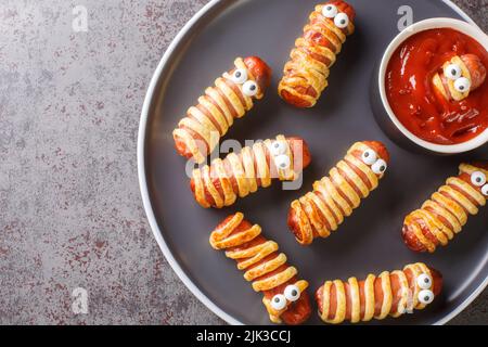 Mummie fatte in casa con ketchup Halloween divertente ricetta del cibo primo piano nel piatto sul tavolo. Vista dall'alto orizzontale Foto Stock