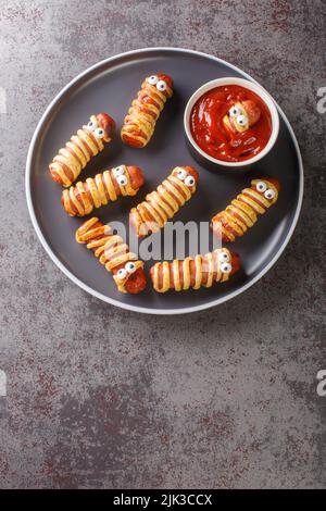 Le salsicce di mamma spaventose nell'impasto con gli occhi divertenti sul tavolo da vicino. Decorazioni divertenti. Halloween alimentare. Vista dall'alto verticale Foto Stock