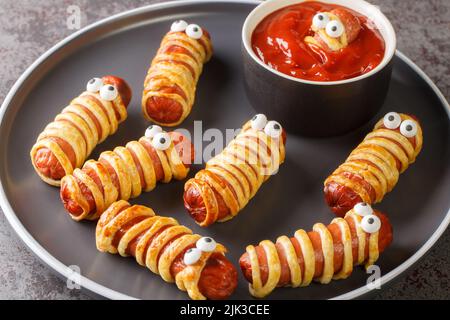 Mummie fatte in casa con ketchup Halloween divertente ricetta del cibo primo piano nel piatto sul tavolo. Orizzontale Foto Stock