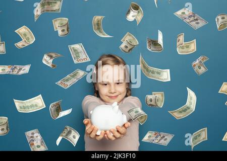 US dollaro denaro pioggia e piggy banca in mano di ragazza carina bambino su blu Foto Stock