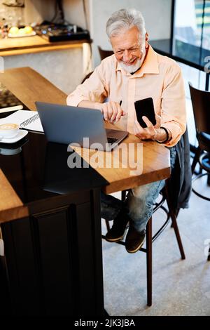 Uno studente temporaneo sorridente seduto in un bar e con una videochiamata in pausa. Studio di studenti senior nel bar. Foto Stock