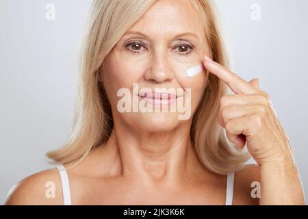 Una bella bionda donna anziana mettere anti-età creme. Fotografia di bellezza Foto Stock