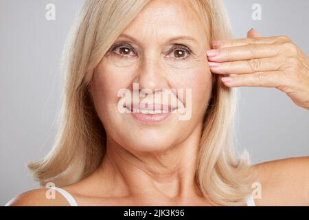 Primo piano di una bella signora anziana che tocca la sua pelle morbida rugosa. Fotografia di bellezza Foto Stock