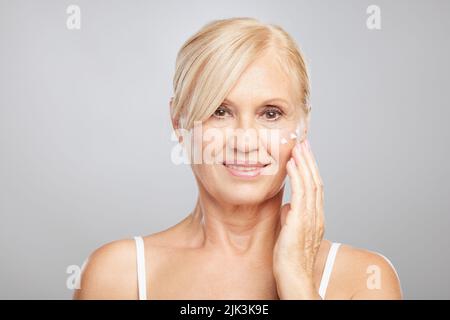 Una bella bionda donna anziana mettere anti-età creme. Fotografia di bellezza Foto Stock