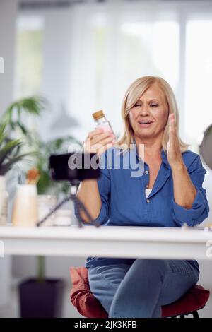 Un vlogger senior seduto a casa e parlando di nuovi prodotti di bellezza. Foto Stock