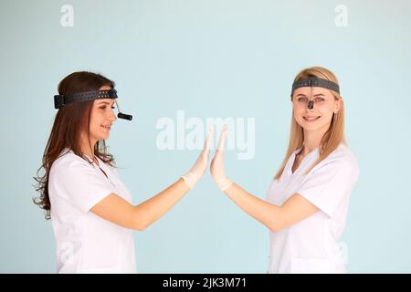 Due otolaringologi femminili sono contenti del lavoro che hanno fatto e stringono le mani su uno sfondo chiaro. Concetto di protezione della salute Foto Stock