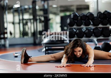 Uno sportivo flessibile sta allungando la gamba in palestra. Foto Stock