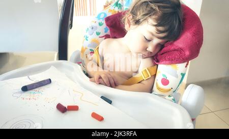 Un bambino piccolo ragazzo bambino addormentato nel suo seggiolone dopo aver giocato con pastelli colorati Foto Stock