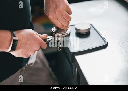 Primo piano del barista che tiene il caffè macinato e manomissioni nel supporto per preparare l'espresso al cliente Foto Stock