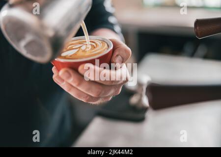 Barista professionale versa il latte in un bicchiere di caffè appena fatto per preparare latte o cappuccino Foto Stock