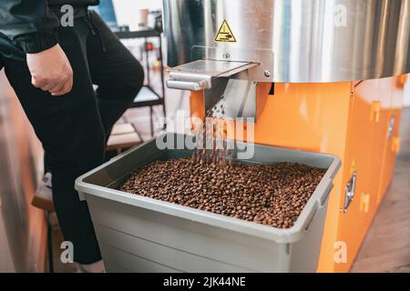 Chicchi di caffè torrefatto dalla macchina tostatrice che si versano nella scatola speciale per la vendita Foto Stock