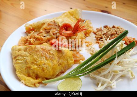 Delizioso Noodle fritto in stile thailandese chiamato Pad Thai avvolto in uova fritte e sormontato da gamberi Foto Stock