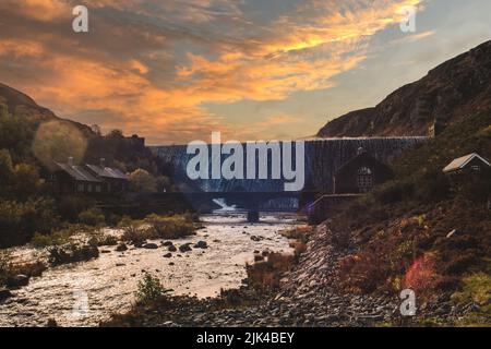 Acqua che scorre sulla diga di Caban Coch nel Galles centrale con il sole tramonta dietro di essa Foto Stock