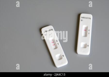 Due kit per test antigenici SARS‑cov‑2 per test automatici con risultati positivi e negativi. Test rapido dell'antigene del coronavirus in una fase, tampone saliva sul dorso grigio Foto Stock