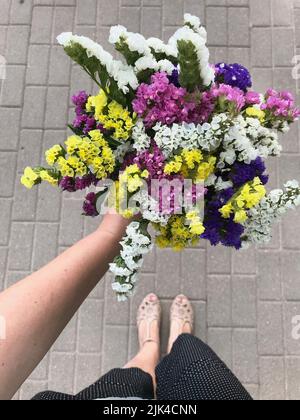 La ragazza tiene nella sua mano tesa un bouquet di fiori statice luminosi. Sparato dall'alto sullo sfondo delle lastre di pavimentazione. Foto Stock