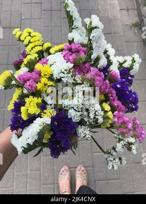 La ragazza tiene nella sua mano tesa un bouquet di fiori statice luminosi. Sparato dall'alto sullo sfondo delle lastre di pavimentazione. Foto Stock