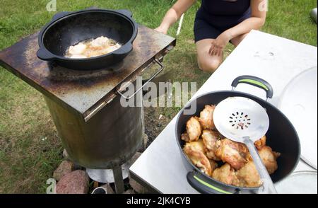 Le cosce di pollo vengono fritte in un calderone in ghisa. C'è fumo e vapore. Nelle vicinanze ci sono pezzi fritti. Cucina all'aperto. Primo piano. Foto Stock