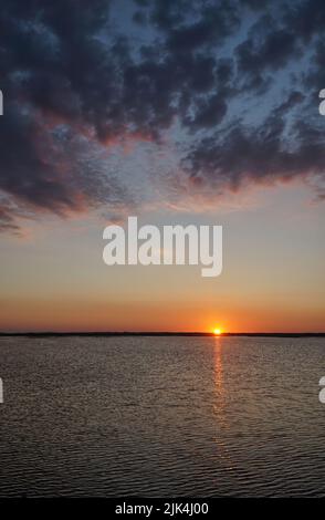 Tramonto sul lago Łebsko, Voivodato Pomeriano, Polonia. Serata estiva, drammatiche nuvole scure nel cielo, il sole si nasconde dietro l'orizzonte, il refl Foto Stock