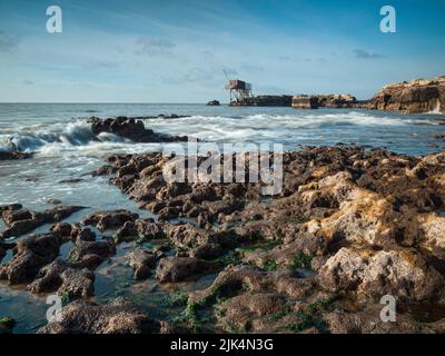 Scena costiera delle onde dell'oceano Atlantico e spiaggia rocciosa con una capanna di pesca all'orizzonte a Saint Palais-sur-mer, Charente Maritime, Francia Foto Stock