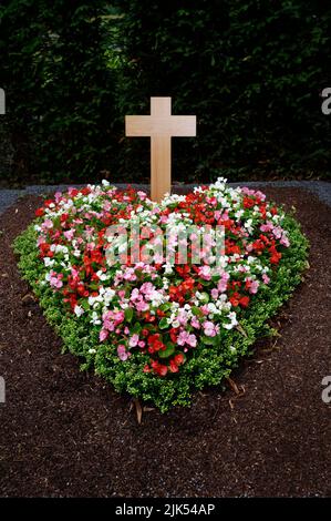 colorato cuore a forma di fiori disposti su una tomba con croce di legno Foto Stock