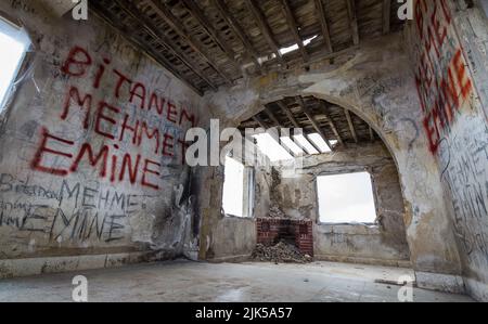 Interno di una vecchia casa abbandonata e vandalizzata con graffiti alle pareti, travi a vista tetto e fori nel tetto. Foto Stock