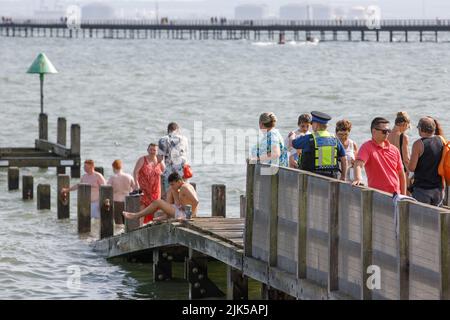 Un ufficiale di supporto della comunità di polizia dice alle persone di scendere da un molo sommerso sulla spiaggia di Southend durante l'ondata di caldo britannica del 2022 Foto Stock