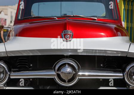 Un camion di pick up su misura Ford F100 anni '50 in rosso e bianco. Vista frontale di parafango, cofano, logo e parabrezza. Foto Stock