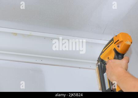 Installazione del soffitto angolo corona stampaggio con l'aiuto di un chiodo pistola ad aria da un falegname Foto Stock