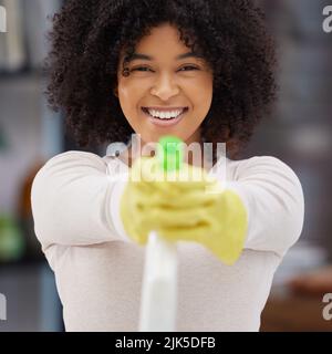 Mani su germi. Una giovane donna attraente in piedi da sola e spruzzare una bottiglia di detergente mentre fa le faccende a casa. Foto Stock