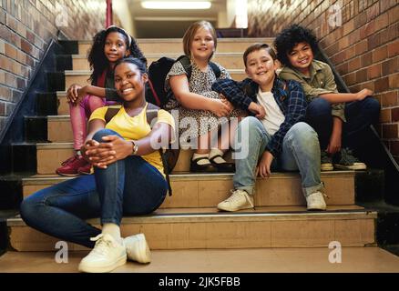 Gli amici fanno divertire la scuola. Sparo a tutta lunghezza di un gruppo di bambini seduti insieme sulla scala a scuola. Foto Stock