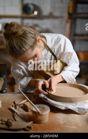 Un ceramista fa un piatto. Donna in grembiule lavora in un laboratorio di ceramica. Foto Stock