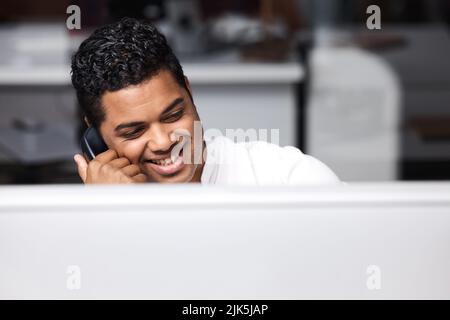 Ha sempre una risposta per voi in un istante. Un giovane uomo d'affari che parla al telefono mentre lavora su un computer in ufficio. Foto Stock