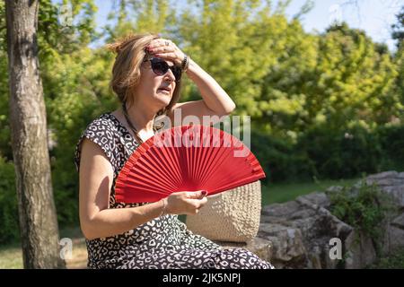 Donna matura che si abbraccia nel parco dalla forte ondata di caldo estiva. Foto Stock