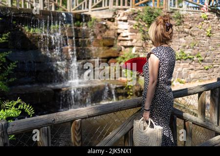 Donna che guarda una piccola cascata di acqua dolce in un parco pubblico in una giornata di sole. Foto Stock