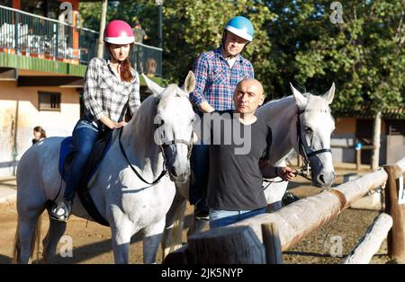 Coppia matura positiva con jockey imparare a cavallo in fattoria Foto Stock