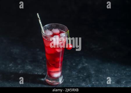 Cocktail fresco di ciliegia rossa con cubetti di ghiaccio in vetro su sfondo nero, da vicino. Bevanda rinfrescante ghiacciata estiva Foto Stock