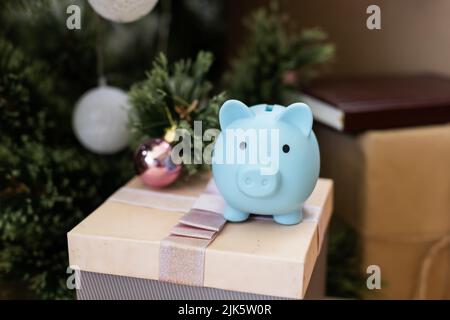 Sotto l'albero di Natale sono scatole con i regali. Sulla scatola c'è una piccola banca di porcellini. Bella carta festiva. Foto Stock