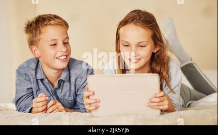 Im sempre cercando di battere i miei fratelli punteggi di gioco. Due bambini piccoli che si trovano sul letto insieme a casa e si legano mentre si utilizza un tablet digitale. Foto Stock