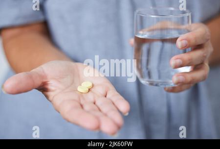 Li prendo ogni giorno. Una donna anziana che tiene un bicchiere d'acqua e due compresse. Foto Stock