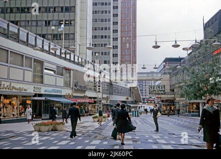 Una vista del quartiere pedonale dello shopping di Sergelgatan o del centro commerciale sotto gli edifici Hötorget (sulla sinistra) nel quartiere centrale di Norrmalm, Stoccolma, Svezia nel 1970. Gli edifici del Hötorget sono cinque edifici modernisti e alti. Norrmalm si trova nel centro di Stoccolma. Negli anni '1950s e '1960s, gran parte del Norrmalm inferiore fu demolita per costruire una città nuova e moderna. Questa immagine proviene da una trasparenza a colori 35mm amatoriale – una fotografia vintage 1970s. Foto Stock