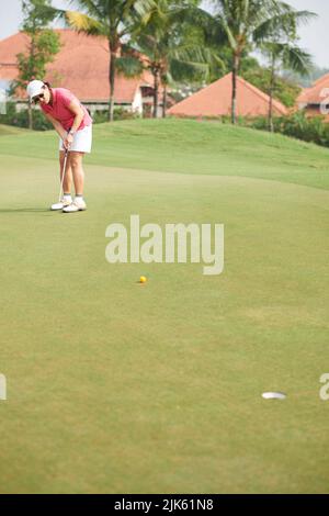 Golfer femminile asiatico guardando la palla che ha colpito Foto Stock