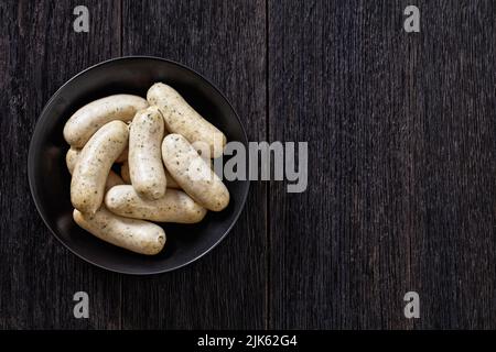 Weisswurst in ciotola nera, salsicce bianche di vitello tritato, pancetta di maiale, spezie e prezzemolo, vista orizzontale dall'alto, giacitura piatta, spazio libero Foto Stock