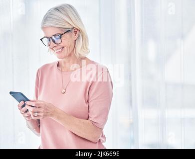 La felicità è a portata di mano, una donna anziana che usa il suo cellulare a casa. Foto Stock