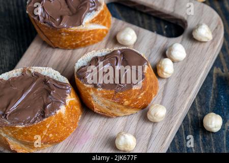 burro di cioccolato spalmato su una baguette, burro di cioccolato dolce spalmato su una baguette durante la preparazione di un semplice dessert a casa Foto Stock