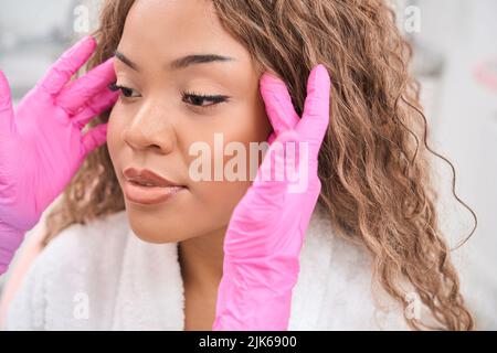 Il cosmetologo esamina il volto del paziente prima della procedura Foto Stock