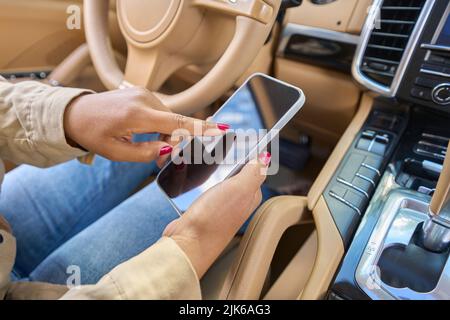 La donna si siede in auto con il telefono in mano Foto Stock