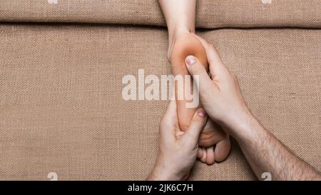 Vista ravvicinata delle mani di un uomo che massaggiano i piedi della donna su tela nel salone termale. Foto Stock