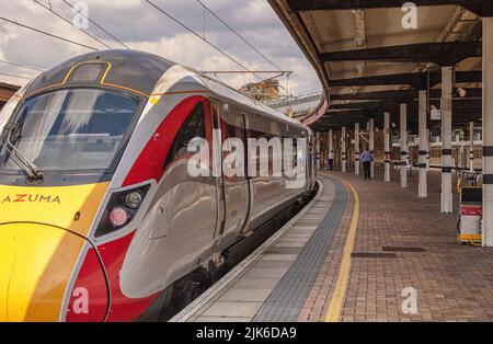 Una moderna locomotiva si trova accanto ad una piattaforma della stazione ferroviaria. I membri dell'equipaggio si trovano vicino alle carrozze e una tettoia in metallo è in testa. Foto Stock