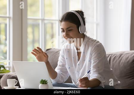 Studentessa indiana positiva in cuffie wireless che fanno videochiamata Foto Stock